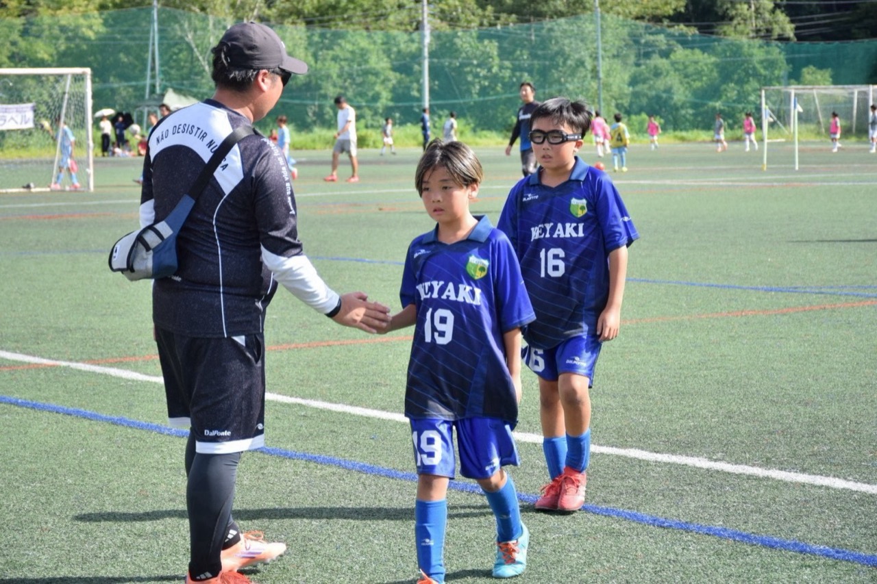 ピッチで選手と手を合わせるけやきSCのコーチ